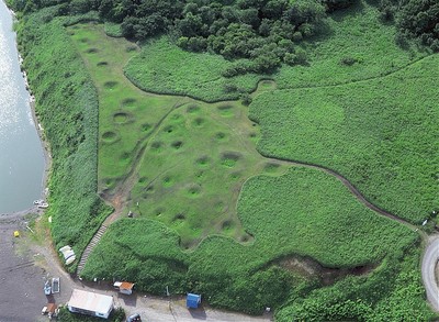 緑一面の草原の中に点在するホロカヤントー竪穴式住居群跡を上空から撮影した写真
