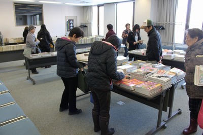 古本・雑誌の還元市で数カ所の平台に積まれた雑誌まわりに町民が集まる視聴覚室の写真