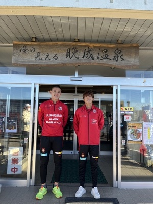 晩成温泉の玄関前でコンサドーレ札幌の赤い服を着ている笑顔の中島選手、金子選手の写真