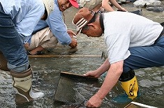 長靴を履いて川の中でゆり板を持って砂金掘りをしている写真