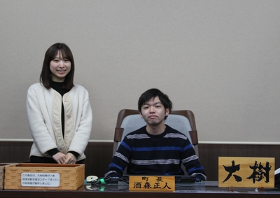 町長の椅子に座っている齋藤大樹さんと横に立っている奥様の写真