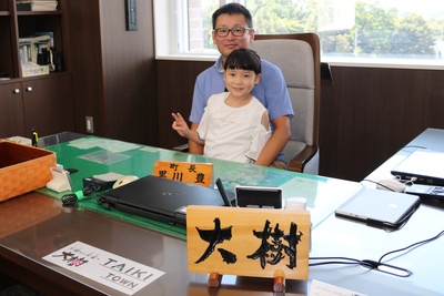 町長の椅子に座って親子で写真を撮っている栗岡大樹さんの写真