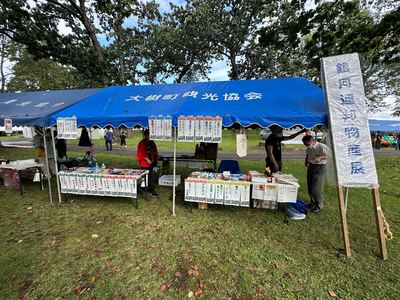 銀河連邦物産展と書かれた看板の隣に立っている青いテントで特産品が用意されている様子の写真