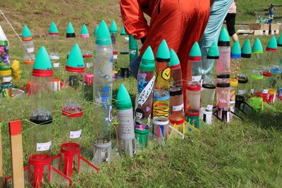 河川敷の草むらに立ち並ぶ、第19回ペットボトルロケットコンテストin大樹にエントリーされたペットボトルロケット群の写真