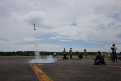 滑走路上にてモデルロケットの発射実験を試みる高校生参加者たちの写真