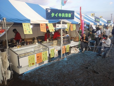 さがみはらフェスタ2011の銀河連邦物産展に出展されたタイキ共和国のブースの写真。パイプ椅子に座って買ったものを食べている人がいる。