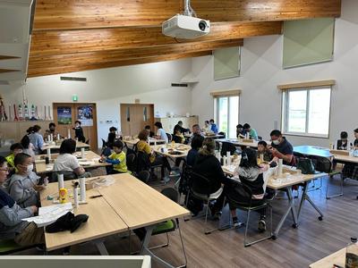 各机にガムテープ、接着剤などが用意されている、大樹分団総会の宇宙交流センターSORA研修室前方からの写真