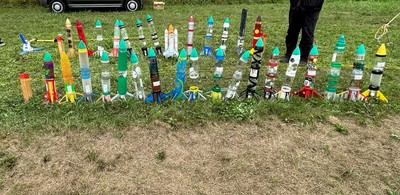 様々な色や長さのペットボトルロケットが芝生の上に集合している様子の写真