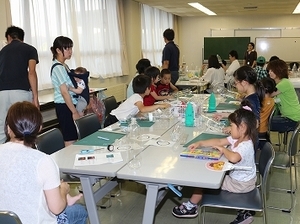 講師の人と大勢の子供たちがロケットの制作をしている写真