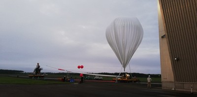 曇り空を背景にした、装置につながれて膨らんでいる白い気球の写真