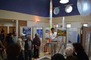 SORAの展示室1にて、職員より多目的航空公園に関する解説を聞く大樹町デイサービスセンターの利用者たちの写真