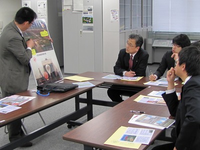 飛行管制棟内の一室にて、着席して職員から多目的航空公園に関する解説を聞く、北海道科学技術振興課・十勝総合振興局地域政策課の各訪問団の写真