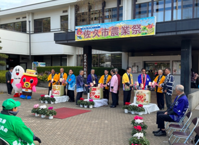 佐久市農業祭と書かれた横断幕が掲げられた建物の前で鏡開きが行われている様子の写真