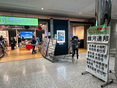 全国観光PRコーナーの前に、「イベント開催中」及び「銀河連邦」と参加自治体について書かれた看板がある様子の写真