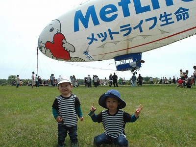 係留中の飛行船スヌーピーJ号を背景に記念撮影に応じる幼児2名の写真