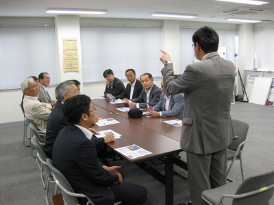 飛行管制棟内の一室にて、着席して職員からの解説を聞く相馬市議会訪問団の写真