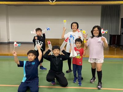 大樹町福祉センターの舞台前で撮影された、風見鶏と傘袋ロケットを持った笑顔の団員たちの写真