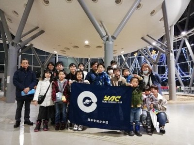 釧路こども遊学館屋内の砂場スペース付近にて記念撮影に応じる研修旅行団の集合写真。中央最前列には団員の児童2名がYACの団旗を掲げている様子が確認できる