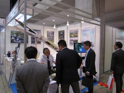 展示物を見ているスーツを着た参加者たちの写真