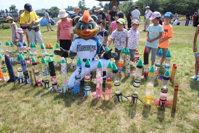 イベントにエントリーされたペットボトルロケット群に囲まれてポーズをとりながら撮影に応じる、日本ハムファイターズのマスコットキャラクター「ブリスキー・ザ・ベアー」の写真
