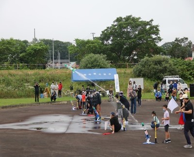 第22回ペットボトルコンテストの競技風景の写真。会場の河川敷広場をペットボトルロケットが勢いよく飛ぶ様子が確認できる