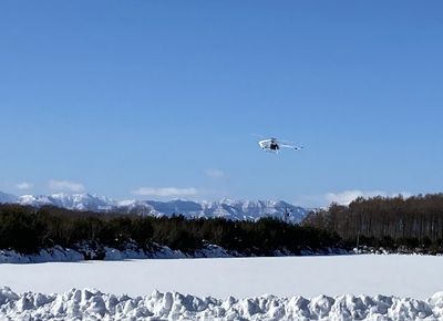 広大な雪原を低空飛行する、三菱重工業のヘリ型無人航空機の写真