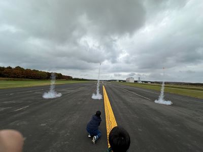 滑走路で白い煙をふきだして垂直に飛び立つモデルロケットの写真