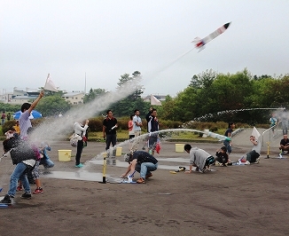 小雨が降るあいにくの天気の中、勢いよく飛んでいくペットボトルロケットの写真