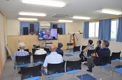 SORAの展示室2にて着席して資料映像を鑑賞する、浦幌活平老人クラブの見学団の写真
