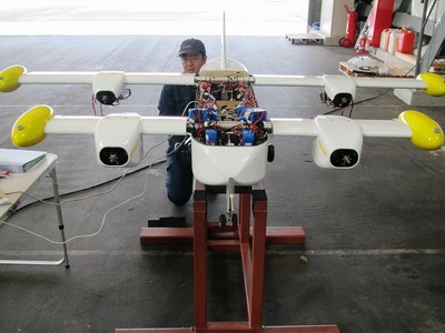 台に乗せられたVTOL無人機が手前側を向いており、胴体部分の上部の外装が外されている写真