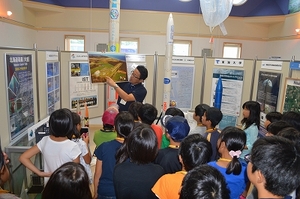 SORAの展示室1にて、職員より多目的航空公園に関する解説を聞く吉岡町使節団の児童たちの写真