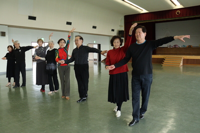体育館でダンスを行っている60歳以上の高齢者の方々の写真