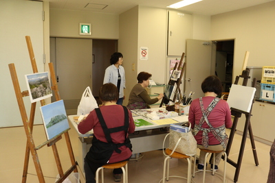 実習室でキャンバスに絵画を描いている60歳以上の高齢者の方々の写真