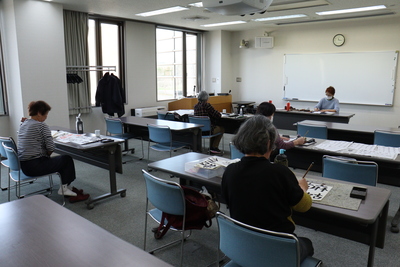 研修室で書道を行っている60歳以上の高齢者の方々の写真