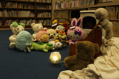 ろうそくの灯る夜の図書館で、子どもたちに預けられたさまざまな可愛らしいぬいぐるみが集まりお泊りする写真