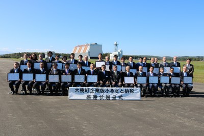 晴天の滑走路上にて記念撮影に応じる、黒川町長と式典参加企業代表者たちの集合写真。各企業代表者の手元にはそれぞれ贈呈された感謝状が確認できる