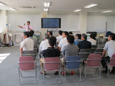 飛行管制棟内の一室にて着席して職員からの解説を聞く、十勝三菱自動車販売株式会社の視察団第2陣の写真