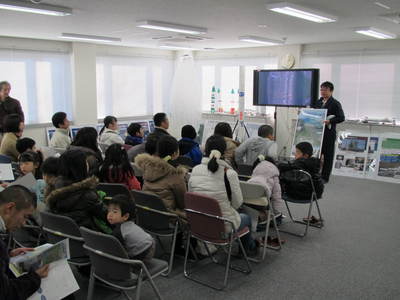 飛行管制棟内の一室にて着席して職員からの解説を聞く、南十勝夢街道モニターツアー参加者たちの写真
