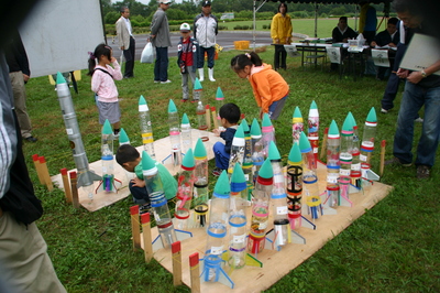 河川敷の一角に立ち並ぶ、第13回ペットボトルロケットコンテストin大樹にエントリーされたペットボトルロケット群の写真