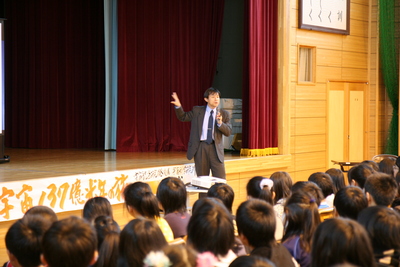 体育館のステージ下にて講演を行う阪本教授の写真