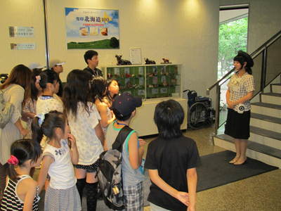 酪農と乳の歴史館の通路にてガイドの案内を聞く旅行団一行の写真