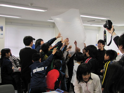 大気球に見立てた大きな袋を膨らませて持ち上げている大樹小学校の生徒たちの写真