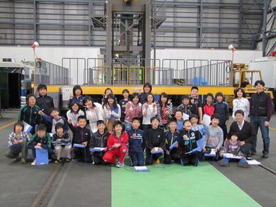 JAXA格納庫内・スライダー式放球装置の前で記念撮影に応じる、大樹小学校6年生の訪問団の集合写真