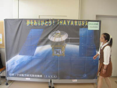 2枚の大型スタンド掲示板上にかけられた、小惑星探査機「はやぶさ」の巨大タペストリーの写真。タペストリーには地球軌道上を飛ぶ「はやぶさ」の画と共に「夢をありがとう！HAYABUSA」の文言も確認できる