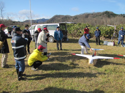 小型無人飛行機の周りに集まり、飛行機の準備いをしている職員の方たちの写真