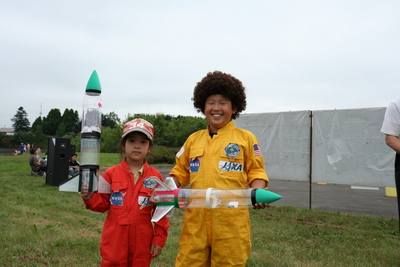 撮影に応じる、コンテストに参加した児童たち男女2人組の写真。両者ともに宇宙服姿で、各々がコンテストにエントリーしたペットボトルロケットを手にしている様子が確認できる