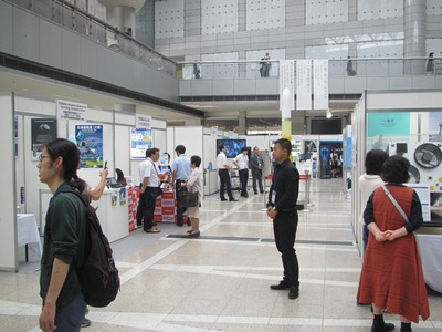 航空宇宙分野のシンポジウムの展示物を見ている人たちの写真