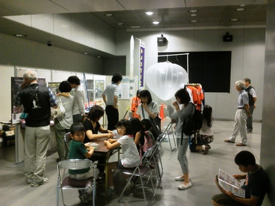 サイエンスパーク2012に参加した出展ブースにて、折り紙でのロケット製作などを教わっている子供たちの写真