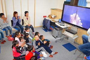 SORAの展示室2に設けられたパブリックビューイングから、H-2Aロケット24号機の打ち上げを見守るYAC分団員たちの写真