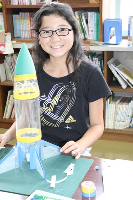 笑顔の児童と机の上の完成したペットボトルロケットの写真